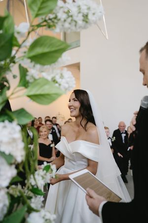 A wedding ceremony with white floral decorations and greenery framing the scene.