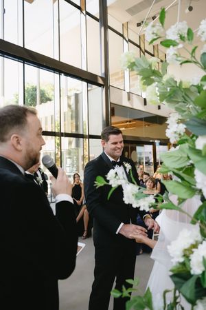 Wedding ceremony with white floral decorations and guests in formal attire in a modern venue.