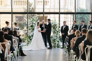 Elegant wedding ceremony setup with rows of white chairs and floral arrangements in a bright indoor venue.