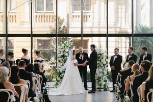 Wide shot of wedding ceremony space with floor-to-ceiling windows and elegant white floral decorations.