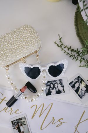 Wedding accessories including pearl necklaces, sunglasses, and gold lettering arranged on white surface.