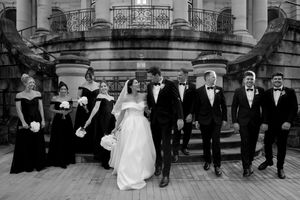Wedding party arranged in formal poses on grand stone steps of historic building.