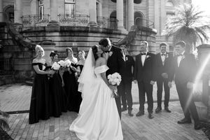 Wedding party posed in front of historic building architecture with classic columns and palm trees.