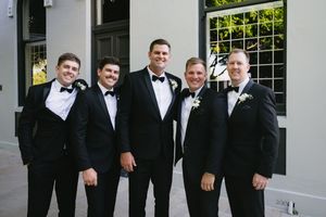 A group of people wearing black tuxedos and bow ties stand together smiling at a formal event.
