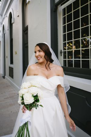 Bride in off-shoulder wedding gown holding white bouquet.