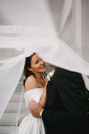 Romantic moment under flowing white wedding veil against light background.