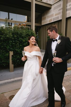 A couple celebrates with champagne, the bride in a white gown and groom in classic black tuxedo.