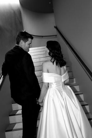 Black and white photo of a wedding couple ascending stairs in formal attire.