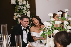 Elegant wedding reception with guests seated at tables decorated with white floral centerpieces and candlelight.