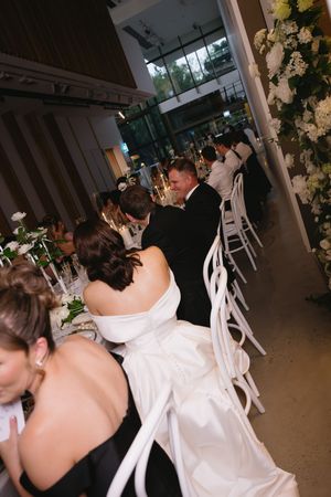 A couple shares their first dance at a wedding reception with white chairs and floral decorations visible in the background.