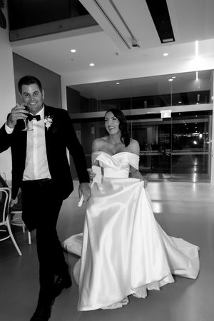 Elegant couple in formal wedding attire walk together in modern indoor venue.