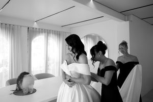 Black and white photo showing people getting ready in a bright room with white curtains and sunlight streaming in.