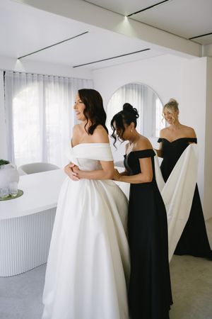 A series of photos showing someone in a white wedding dress being helped by an attendant in black.