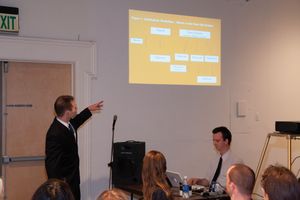 Yellow presentation slide projected on screen during business meeting with audience visible.