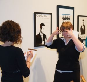 Group viewing and interacting with photographs displayed on a white gallery wall.