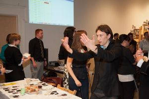 People gathered around tables in a bright meeting room with a projection screen visible.