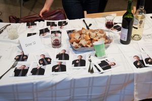 Long table set with wine glasses, plates and photographs laid out for an event.