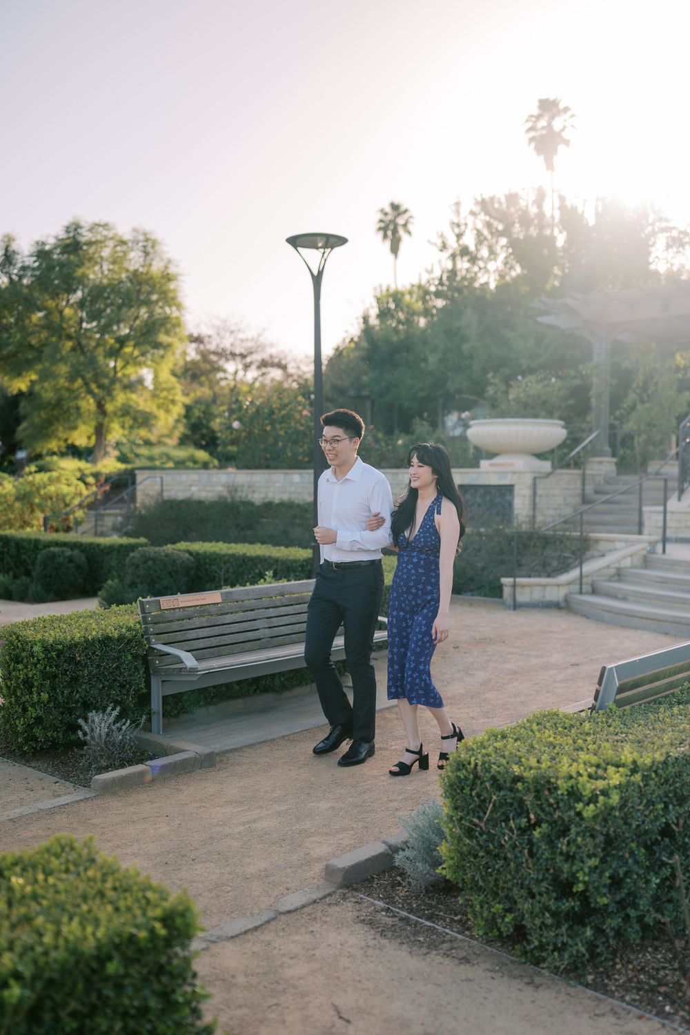 A couple walks together in a serene garden path during golden hour sunlight.