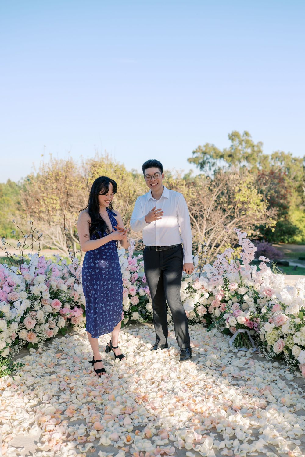 A couple shares a romantic moment in front of a beautiful floral arch with pink and white flowers.