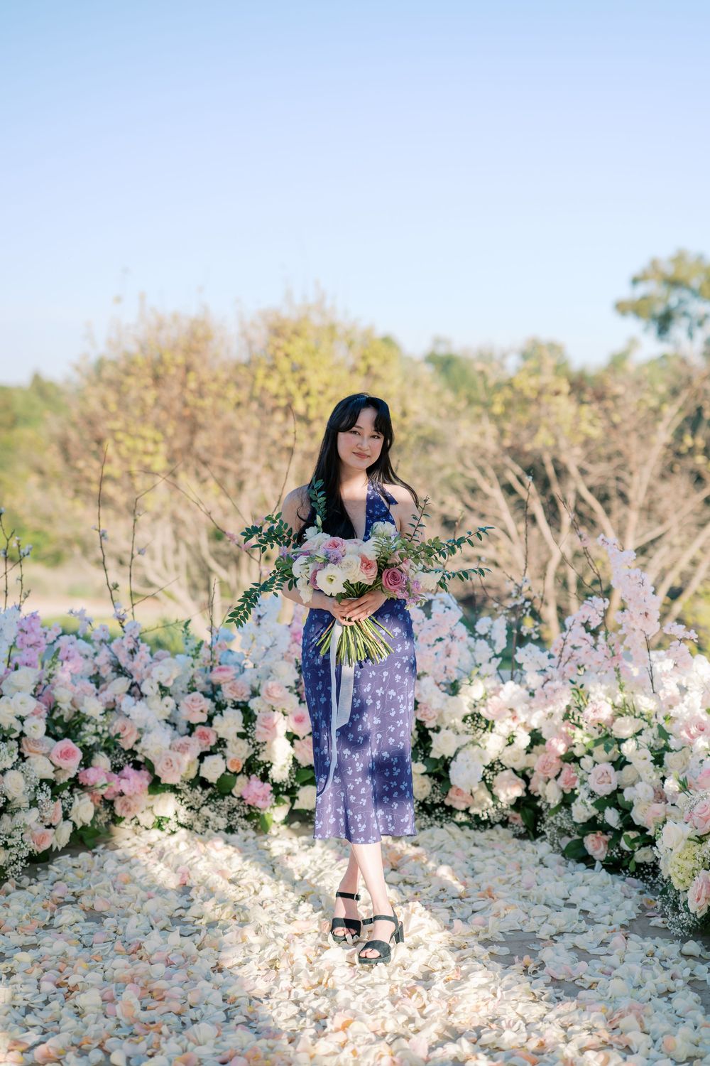 A romantic garden photoshoot featuring a purple floral dress among a beautiful flower arch display.