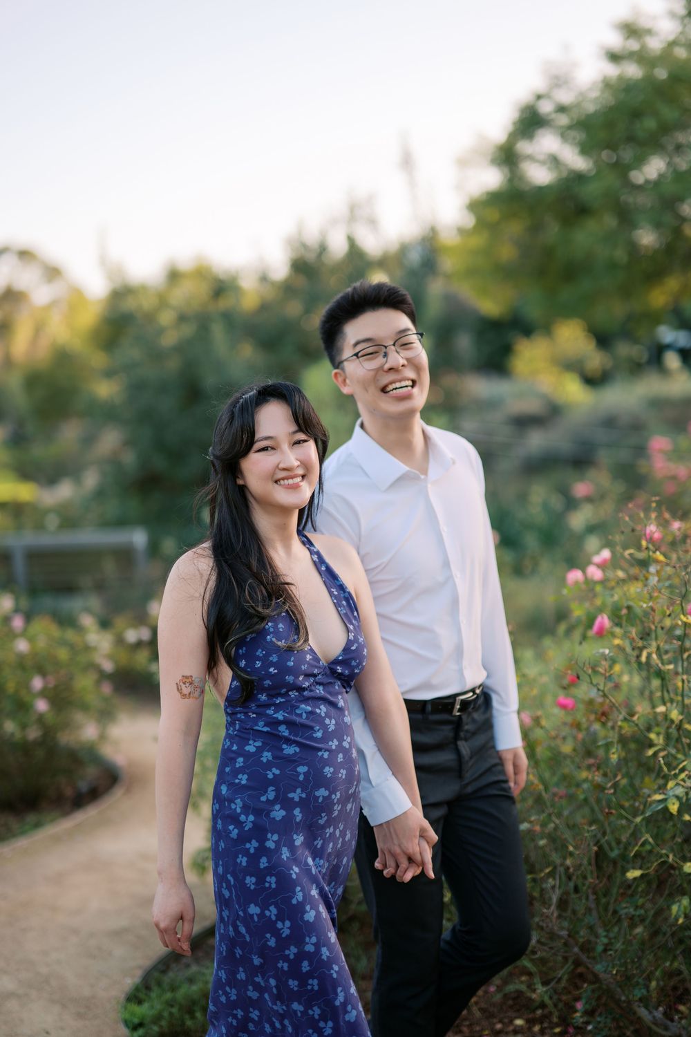 Two people share joyful moments together on a garden pathway surrounded by flowers.