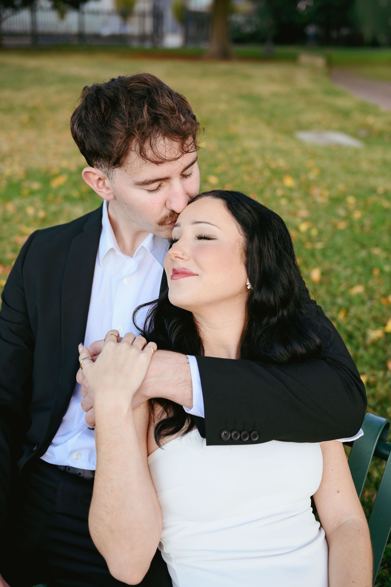 A romantic couple embraces on a park bench surrounded by autumn leaves on a peaceful afternoon.