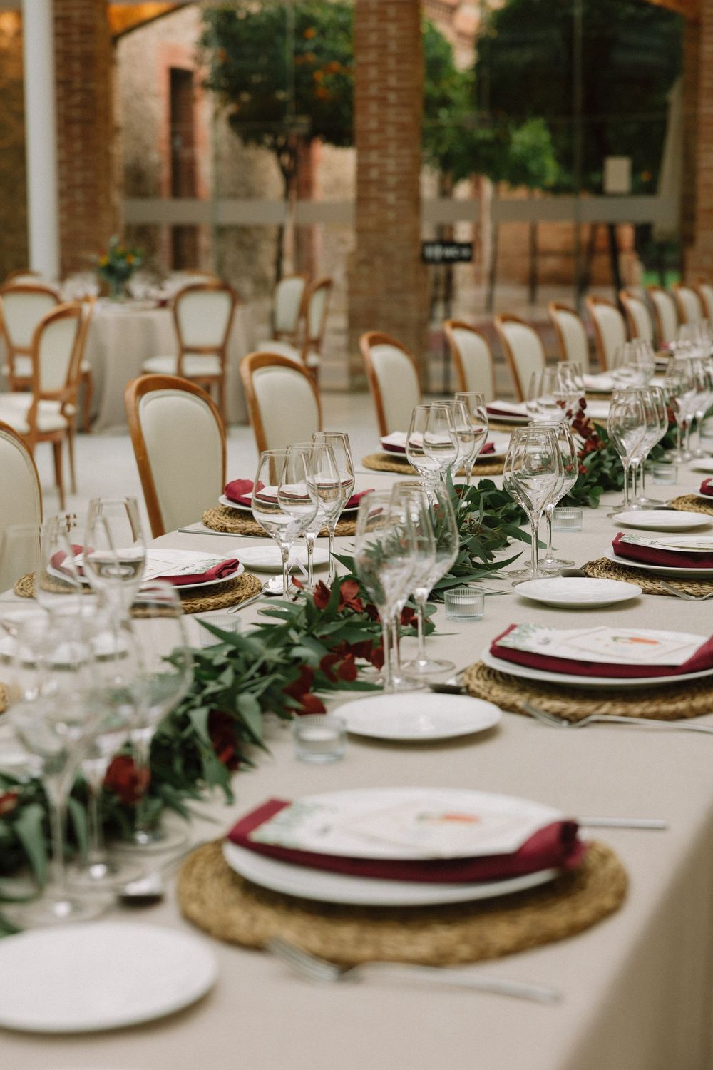 Elegant table setting with burgundy napkins, gold chargers, and eucalyptus garland runner at wedding reception Can Magí Sant Cugat.