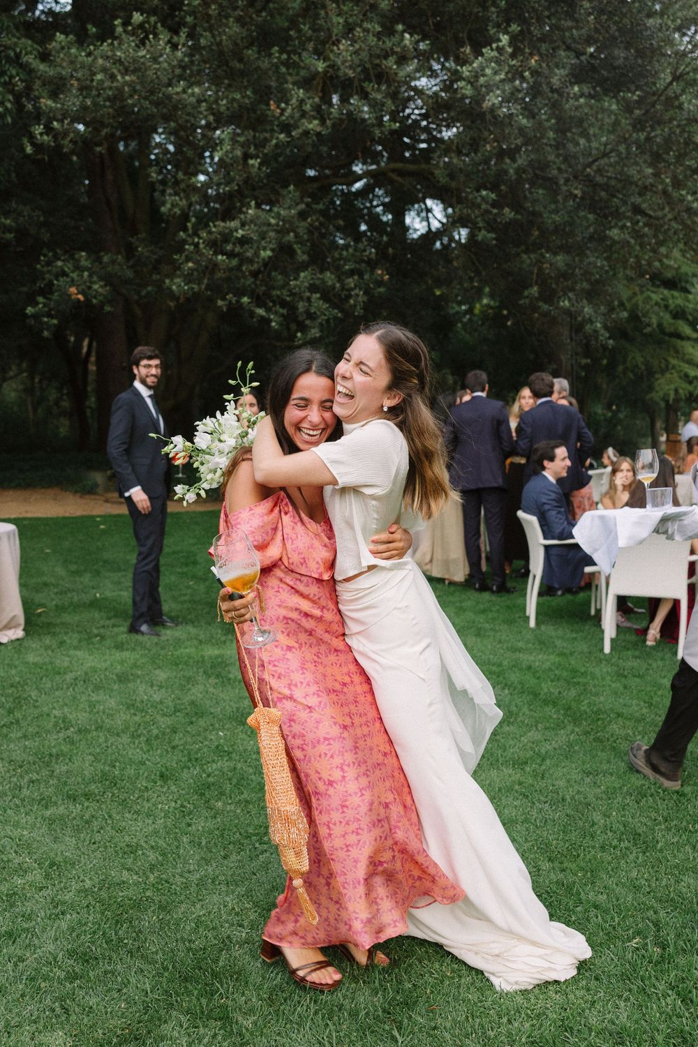 A joyful moment captured at an outdoor wedding celebration as two guests embrace on a grassy lawn Castell de Perelada.
