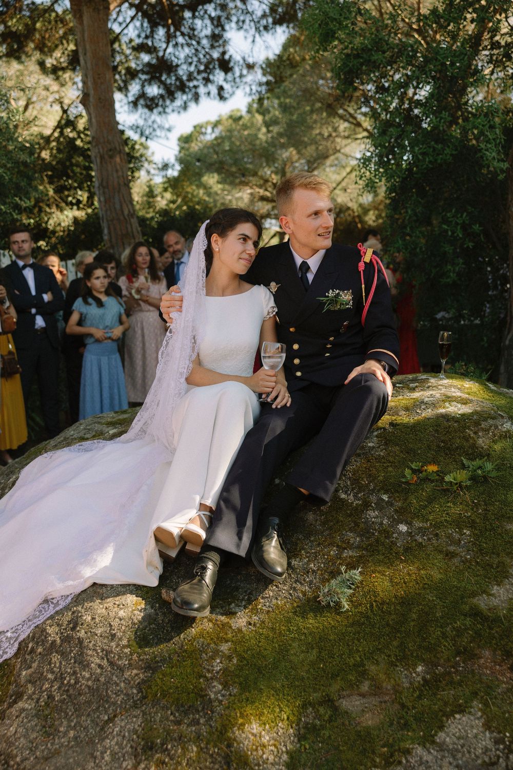 Wedding couple sits on mossy rocks surrounded by trees.