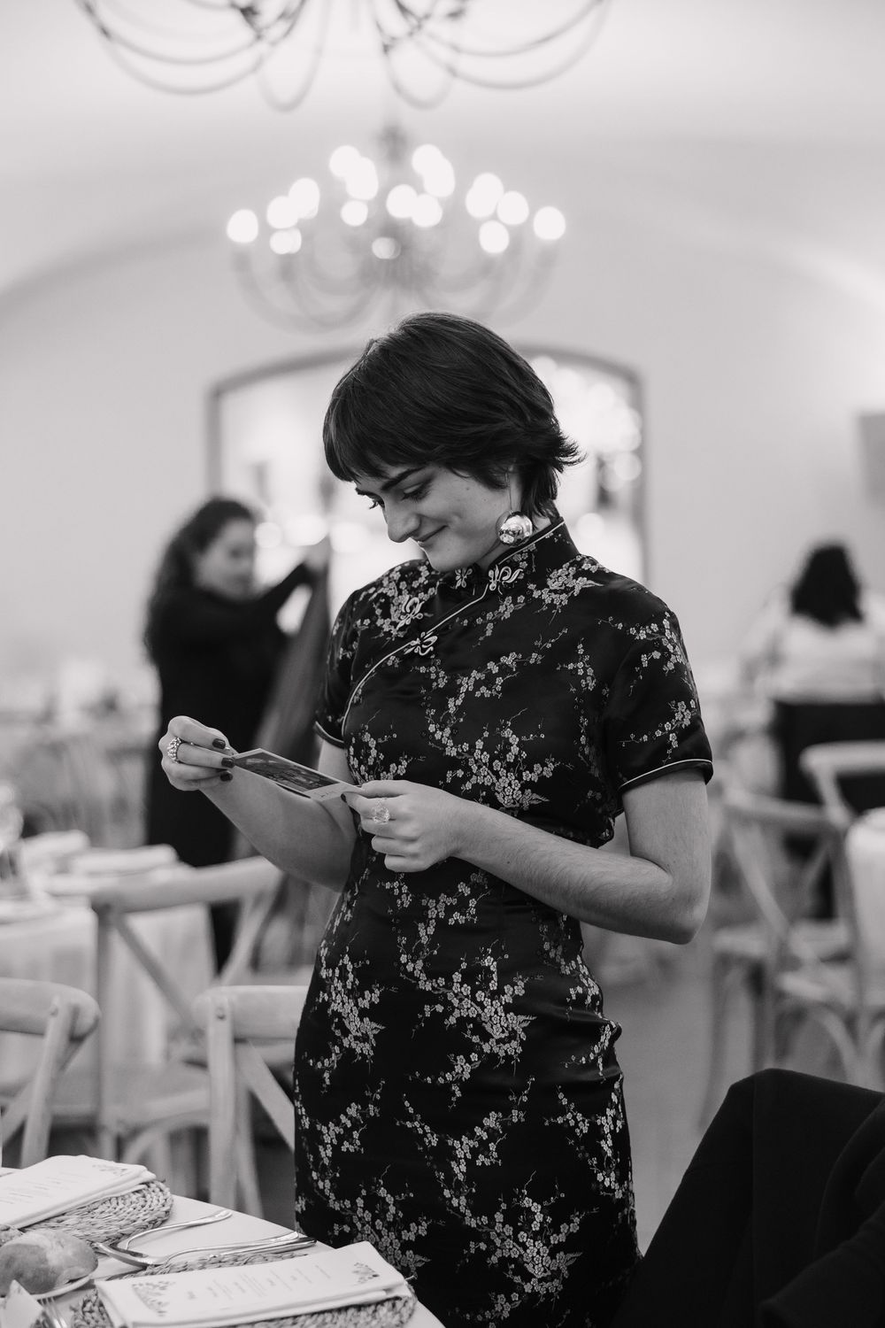 Person in black lace dress examining something in an elegant white room with chandeliers Masía Ca n'illa La Garriga