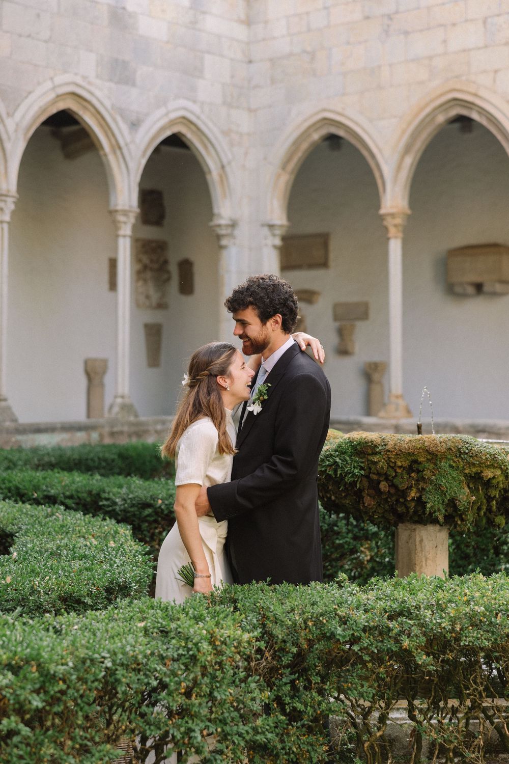 Couple sharing intimate moment in monastery garden with stone arches Castell de Perelada.