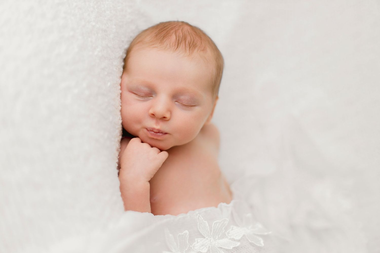 A tiny baby wrapped in soft pink blankets gazes upward with bright eyes.
