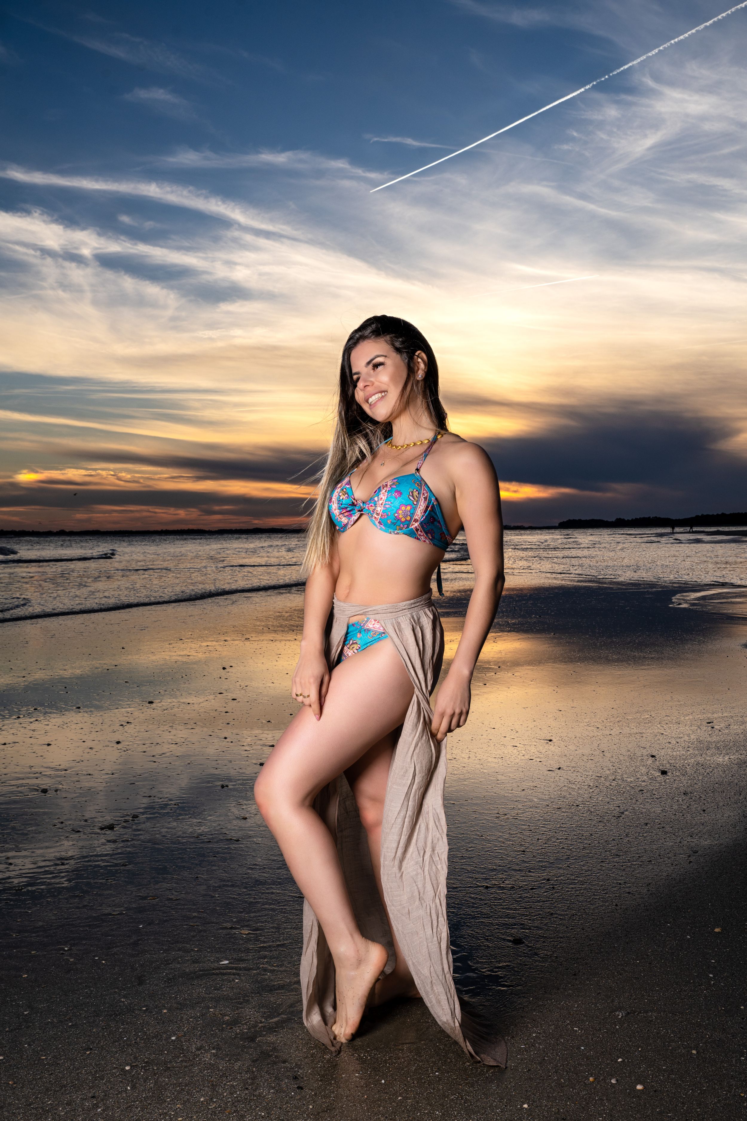 A beachwear photoshoot at sunset with dramatic clouds and ocean backdrop on a sandy shore.