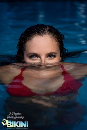 Close up of swimmer partially submerged in blue pool water wearing red swimwear.