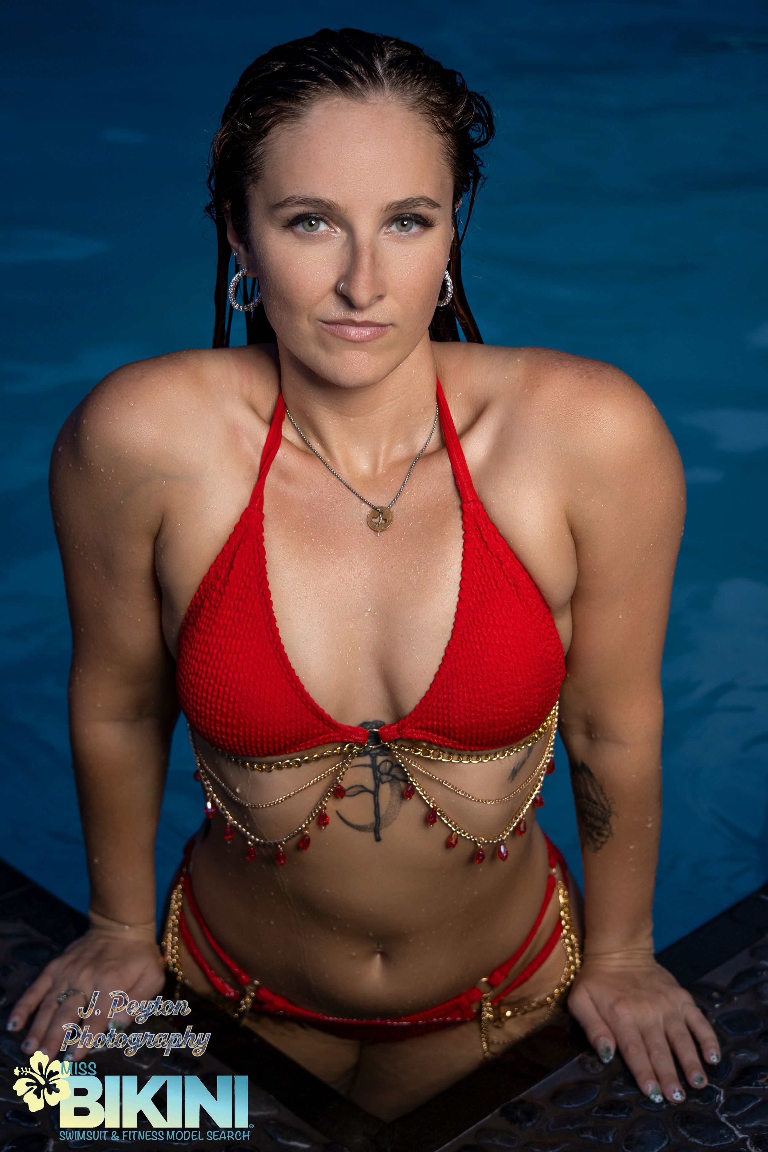 Woman in red bikini poses in swimming pool with dark blue water background.