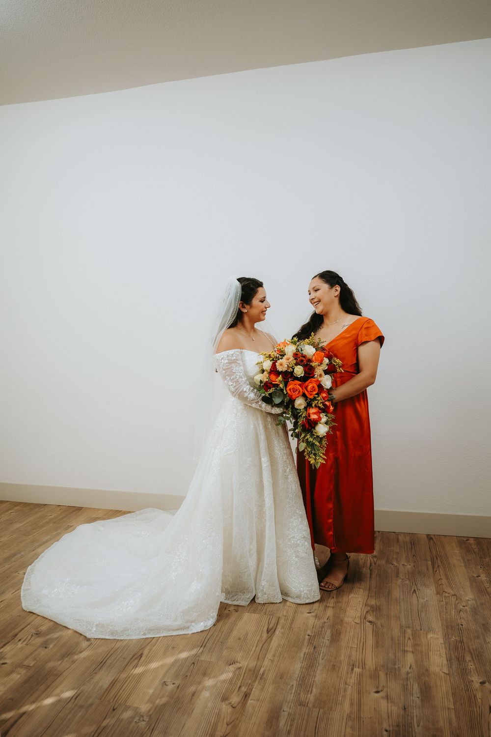 Two people in a white wedding dress and red dress share joyful moments together on a wooden floor.