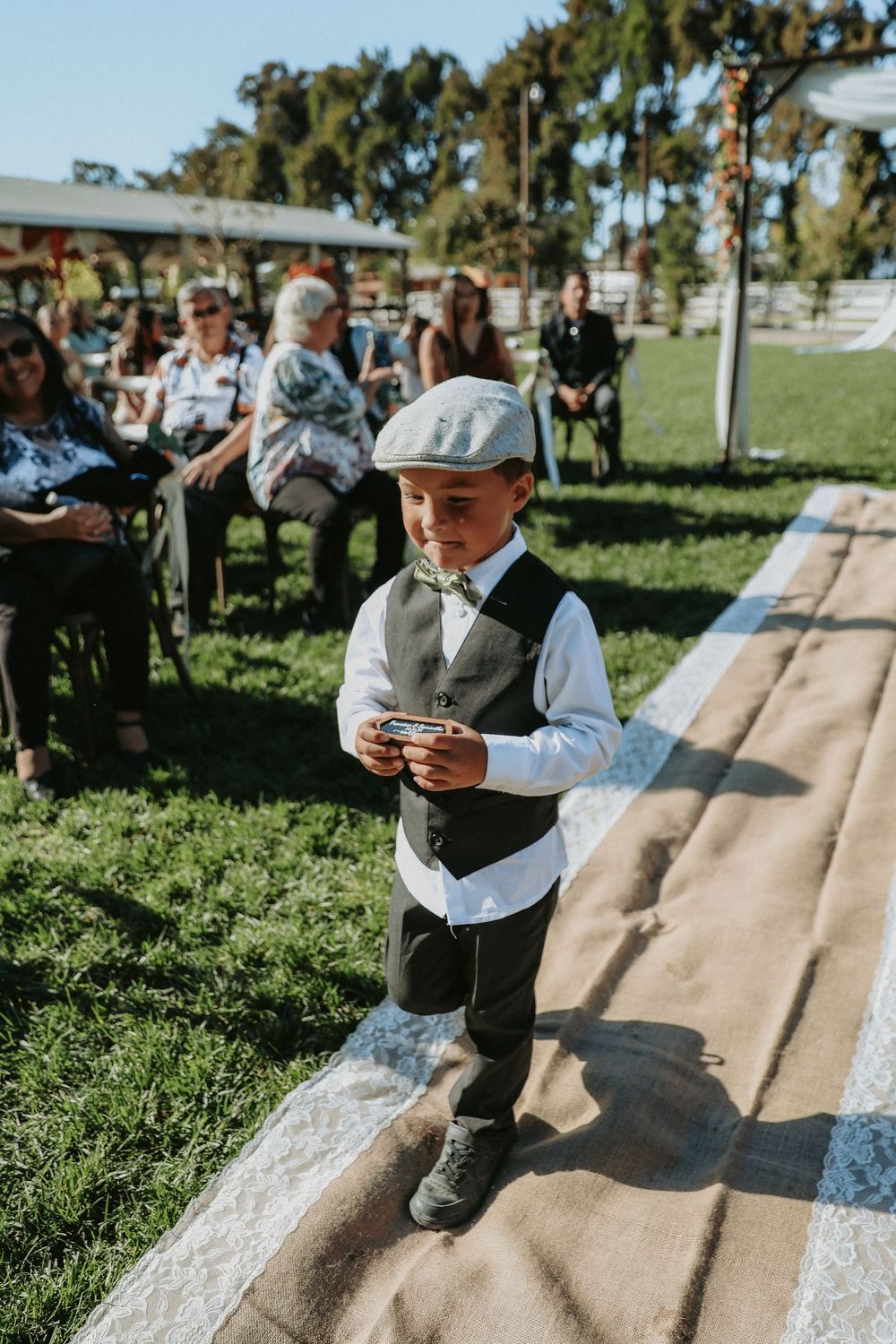 A young boy in formal attire plays on a concrete slide in a sunny outdoor setting.