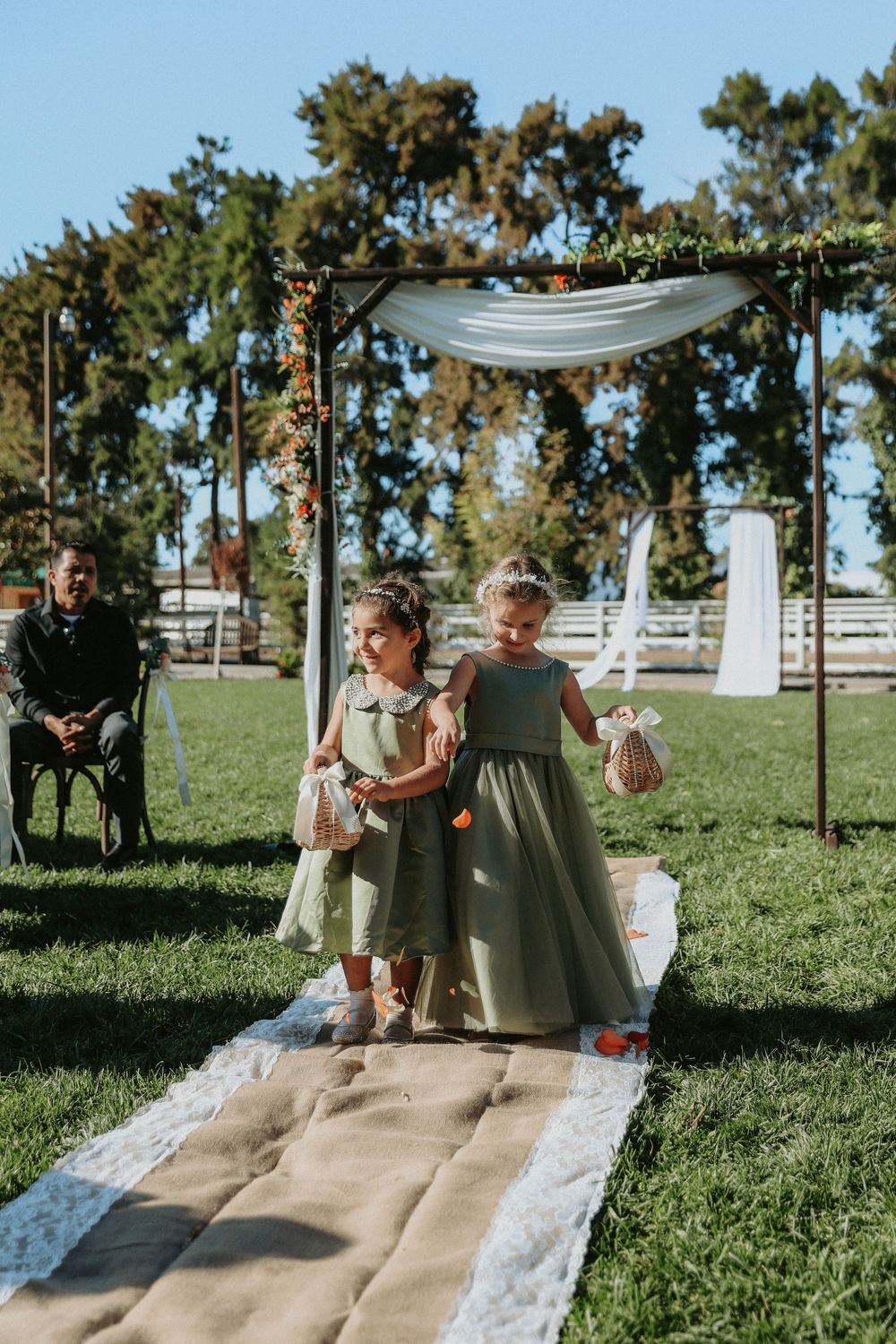 Young children play on a white aisle runner on grassy lawn at outdoor wedding venue.