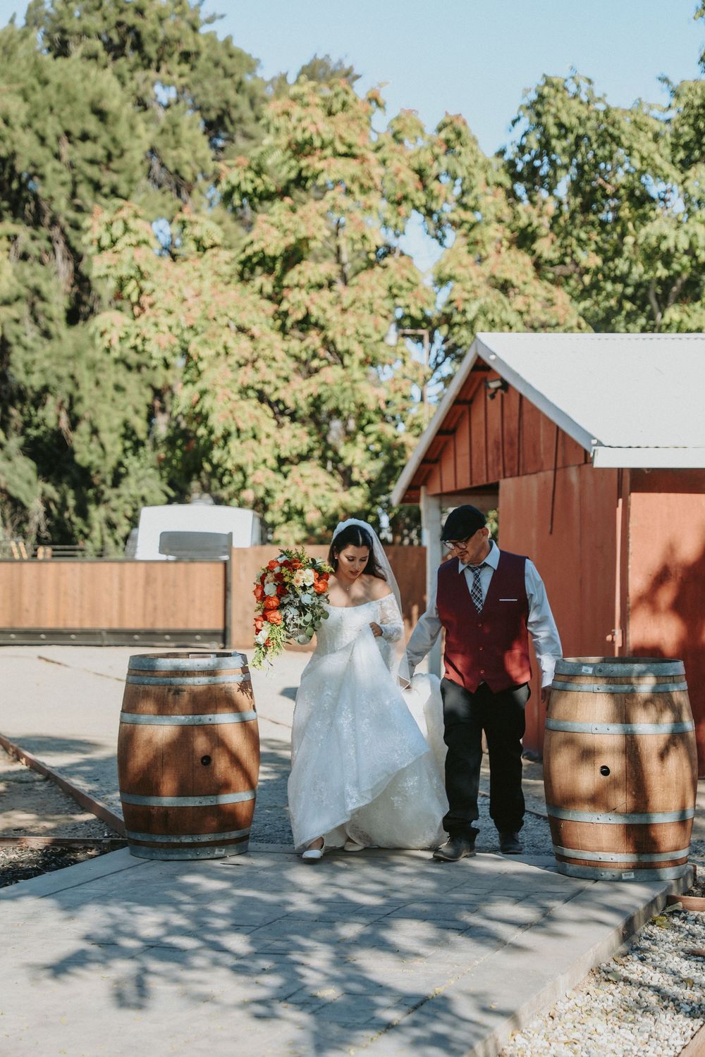 A wedding scene with wooden barrels and rustic decor against a red barn backdrop.