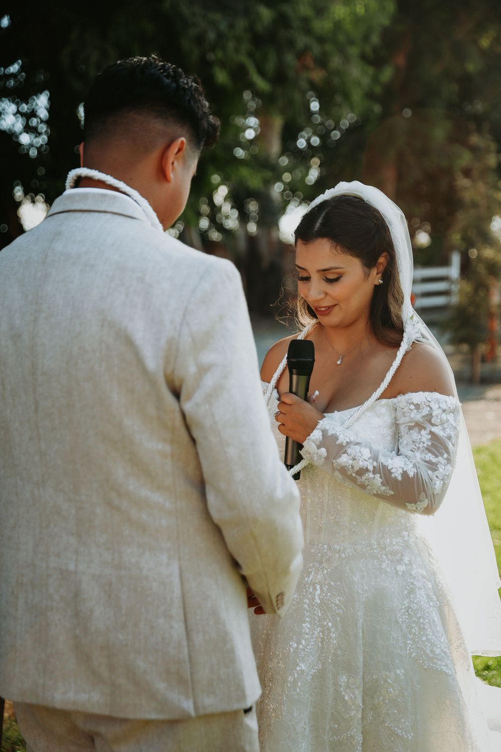 A romantic wedding couple shares an intimate moment in a garden setting, with the bride wearing a lace gown.