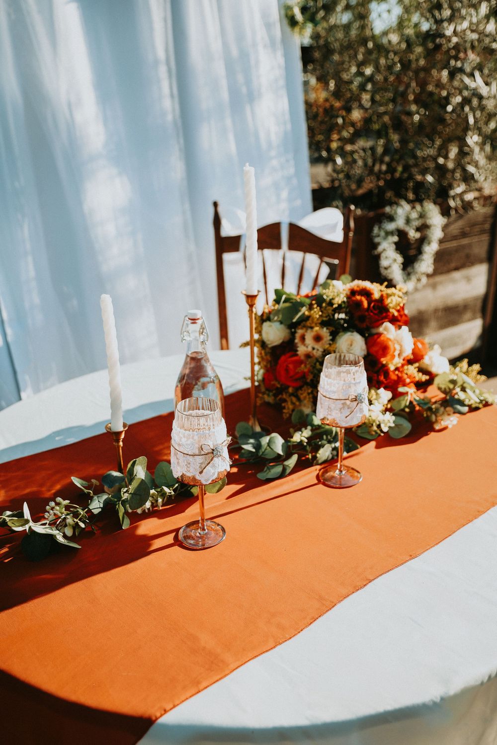 A series of elegant table settings with orange runners and floral centerpieces against light blue drapes at a wedding reception.