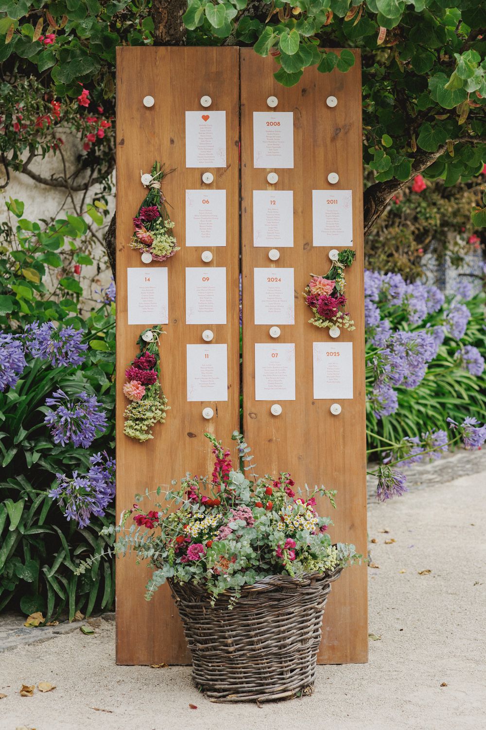 Rustic wooden seating chart display boards with floral arrangements in wicker baskets at an outdoor garden at Quinta Valle do Riacho
