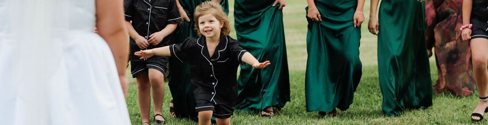 Wedding party members in emerald green dresses gather around on grass during outdoor ceremony.