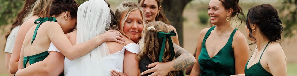 Bridesmaids in emerald green dresses share joyful embrace during outdoor celebration.
