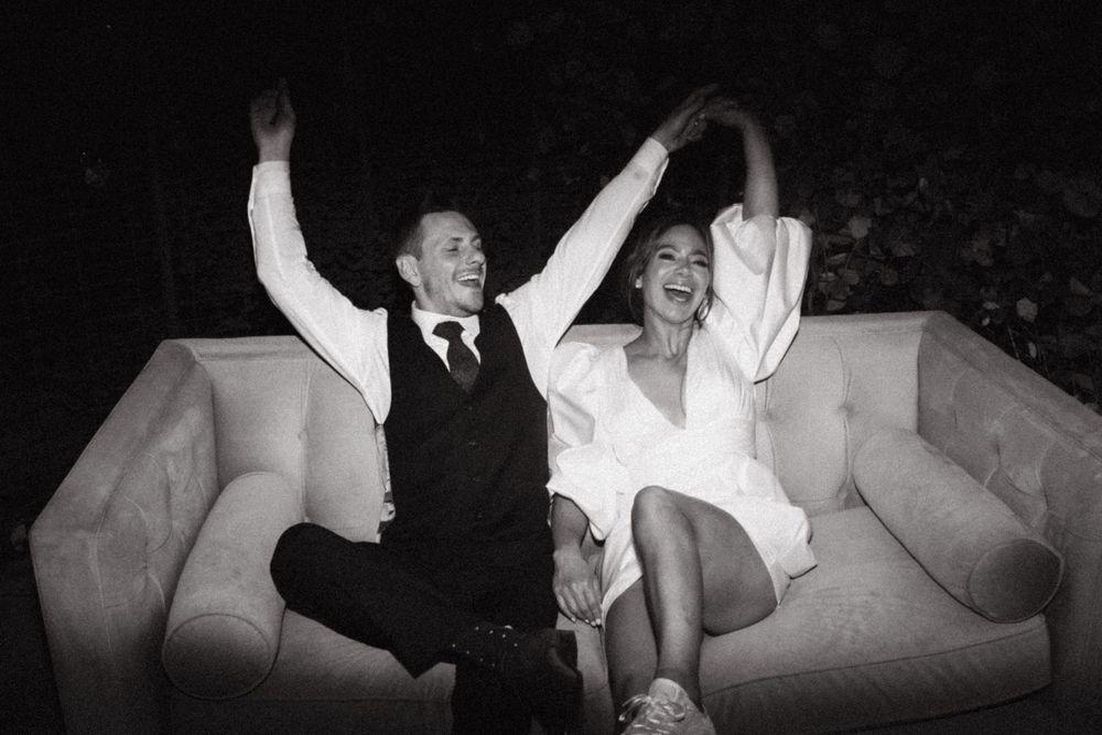Wedding reception guests celebrate joyfully on white couches.