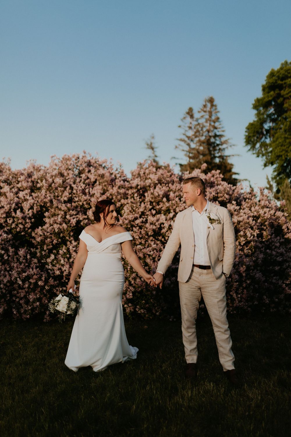 Wedding couple poses in front of blooming pink cherry blossoms at sunset.