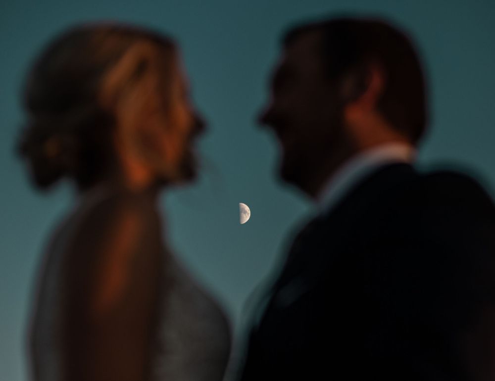 Silhouetted couple against dusky blue sky with crescent moon.