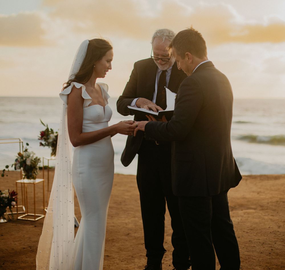 Intimate beach wedding ceremony at sunset with golden light illuminating the coastline.