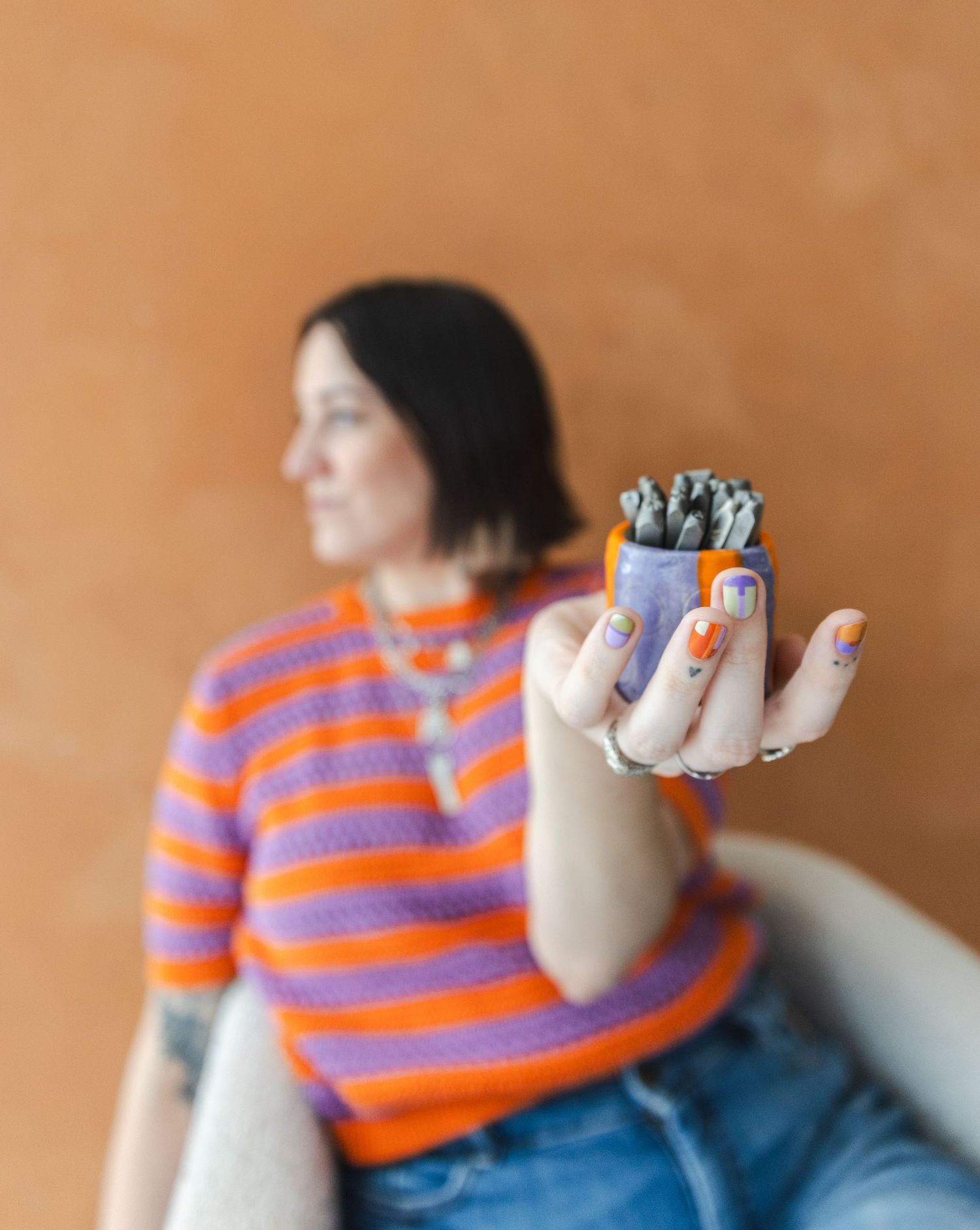 A person in an orange and purple striped sweater gestures expressively in a sequence of candid poses against a brown wall.