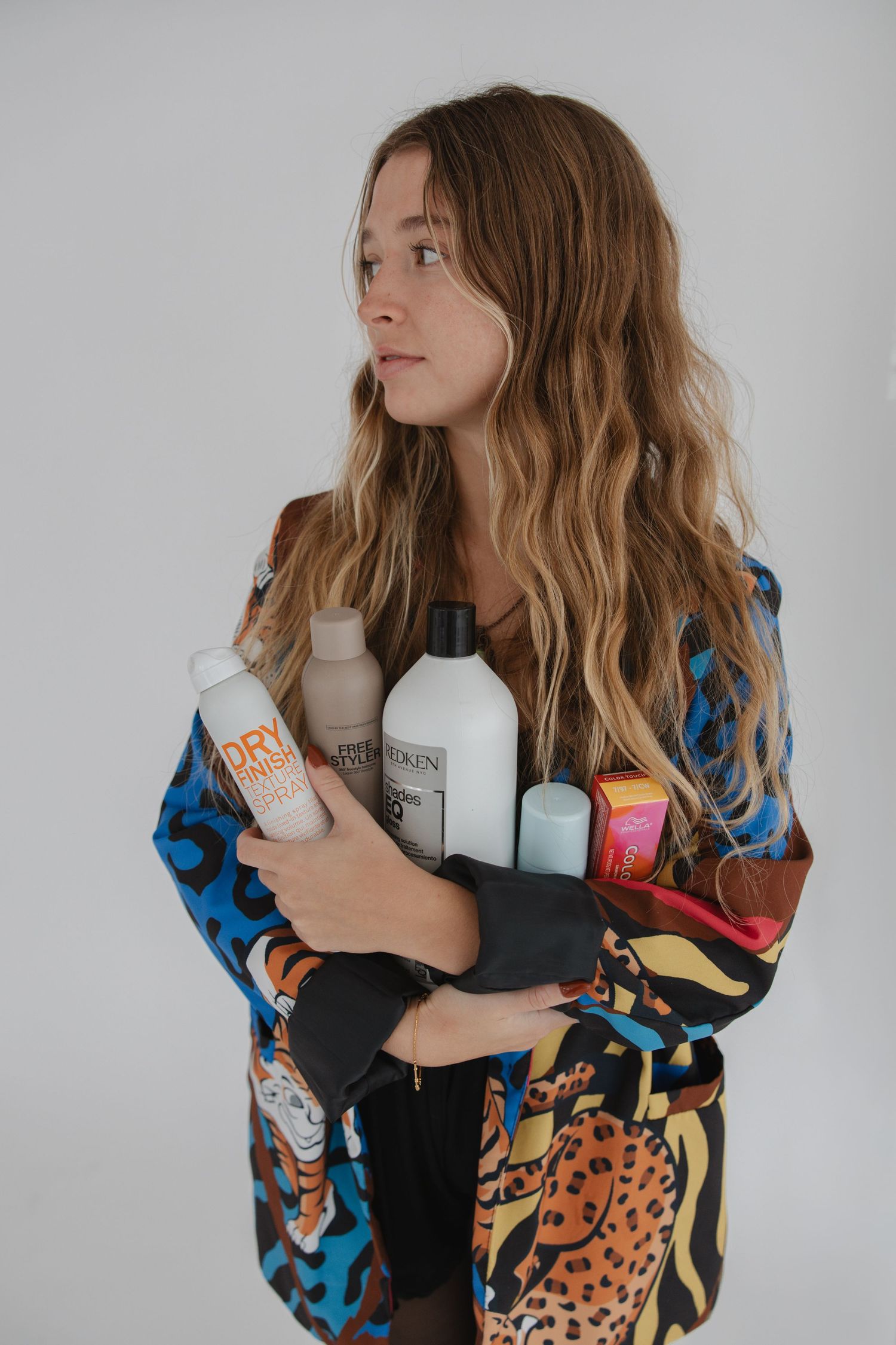 Model in colorful animal print robe holds beauty products against white background in lifestyle product photoshoot.